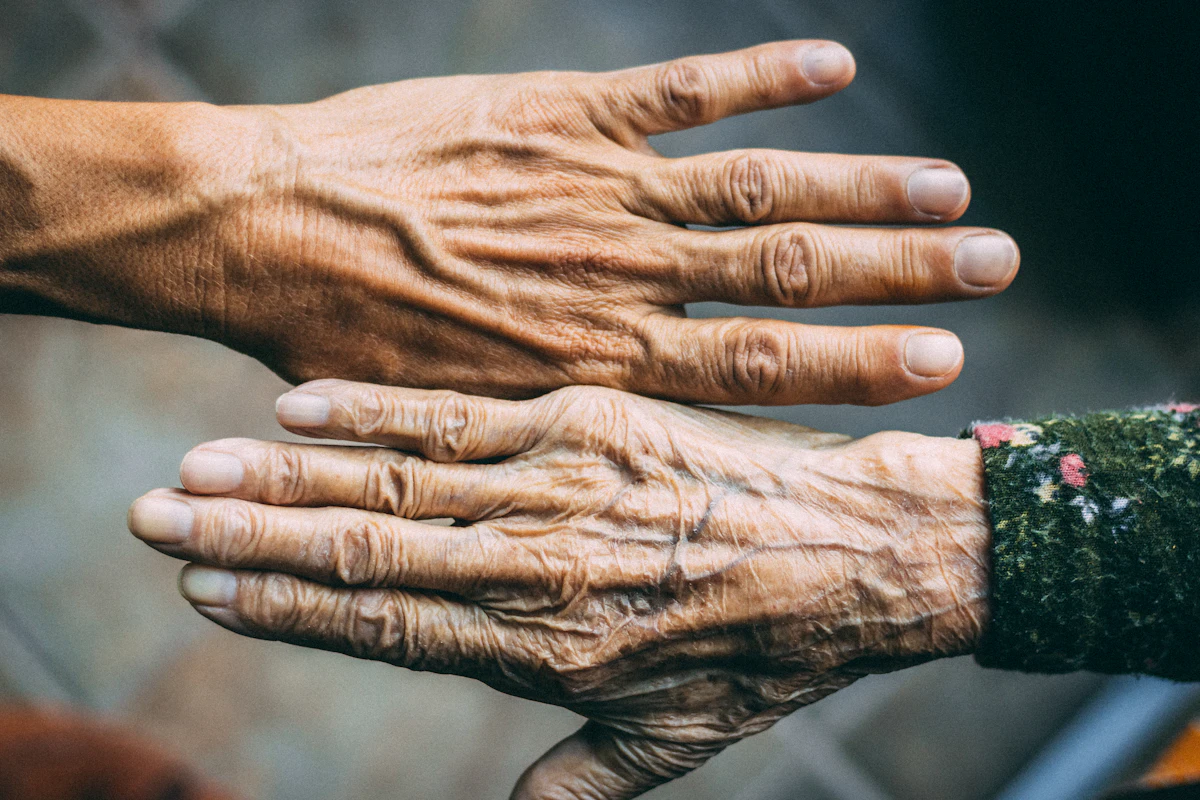 A younger hand rests on top of an older, lined hand whose arm is in a dark floral sleeve.